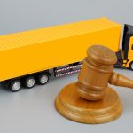 Wooden gavel and yellow cargo truck on grey background.