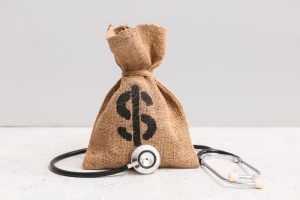 Money bag with stethoscope on table against grey background