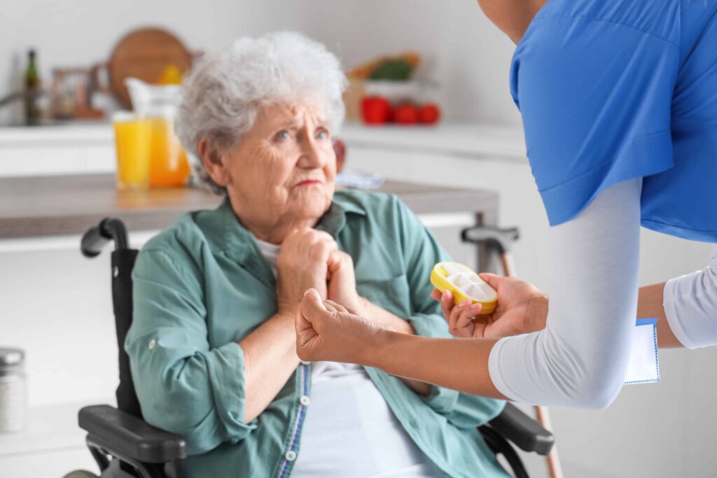 Elderly woman in wheelchair looking concerned as a caregiver offers her medication at home Elderly woman in wheelchair looking concerned as a caregiver offers her medication at home