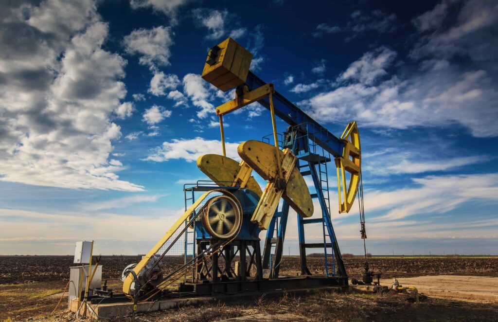Oil pump jack operating in an open field under a blue sky representing oil field work and industrial operations. Oil pump jack operating in an open field under a blue sky representing oil field work and industrial operations.